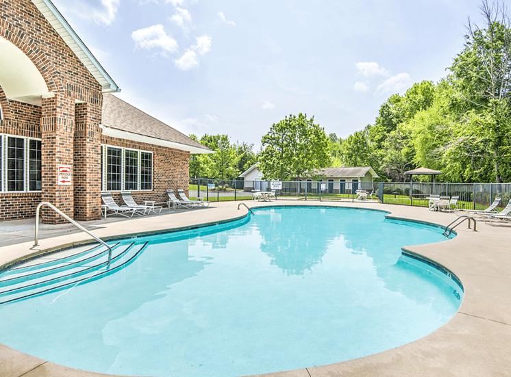 Leasing Office Exterior with Swimming Pool and Sun Deck with Lounge Chairs Near Tree-line